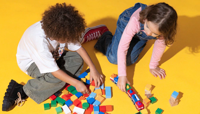 Dos niños jugando con bloques de colores sobre un piso amarillo